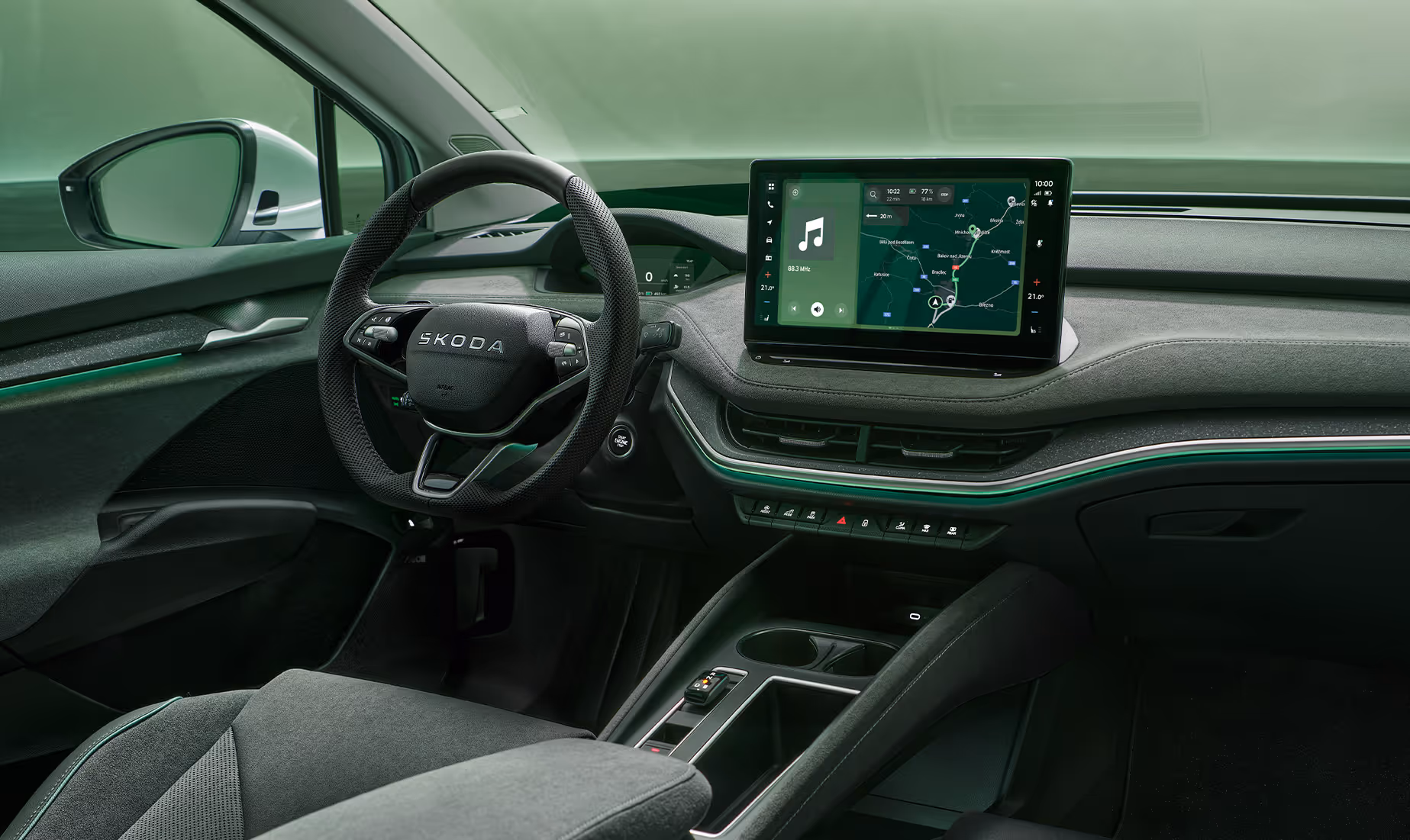 Fokus auf das Armaturenbrett und das Infotainmentsystem des Škoda Enyaq. Zentral platziert ist das freistehende 13-Zoll-Infotainmentdisplay, das eine Navigationskarte und diverse Fahrzeugfunktionen anzeigt. Das dunkle Interieur der Design Selection „Lodge“ wird durch eine grüne Ambientebeleuchtung abgerundet. Unten rechts steht auf einer dunkelgrün abgesetzten Fläche der Schriftzug "Škoda Connect".