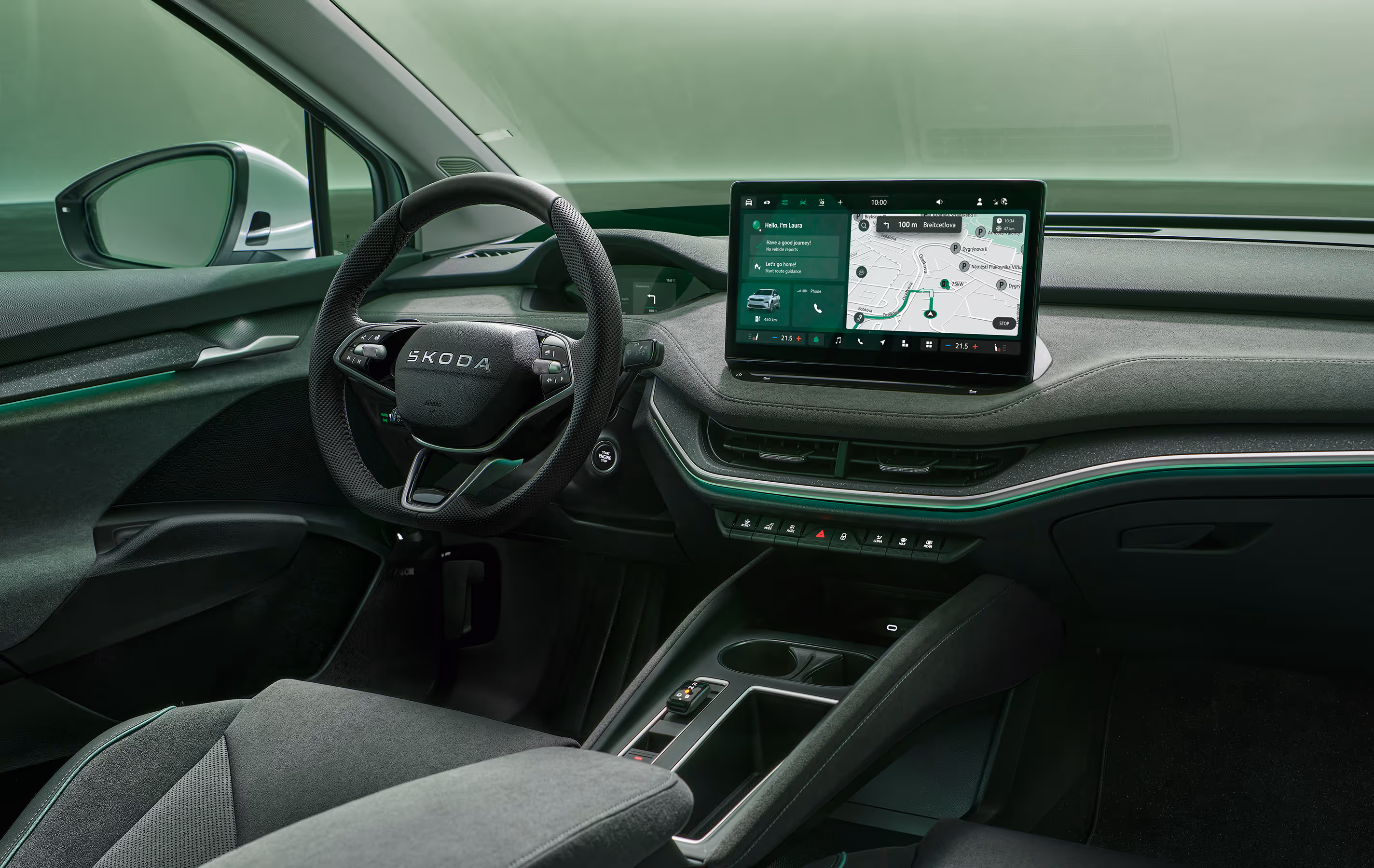 Fokus auf das Armaturenbrett und das Infotainmentsystem des Škoda Enyaq. Zentral platziert ist das freistehende 13-Zoll-Infotainmentdisplay, das eine Navigationskarte und diverse Fahrzeugfunktionen anzeigt. Das dunkle Interieur der Design Selection „Lodge“ wird durch eine grüne Ambientebeleuchtung abgerundet. Unten rechts steht auf einer dunkelgrün abgesetzten Fläche der Schriftzug "Škoda Connect".