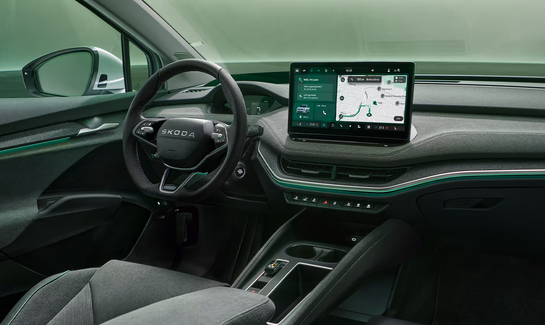 Fokus auf das Armaturenbrett und das Infotainmentsystem des Škoda Enyaq. Zentral platziert ist das freistehende 13-Zoll-Infotainmentdisplay, das eine Navigationskarte und diverse Fahrzeugfunktionen anzeigt. Das dunkle Interieur der Design Selection „Lodge“ wird durch eine grüne Ambientebeleuchtung abgerundet. Unten rechts steht auf einer dunkelgrün abgesetzten Fläche der Schriftzug "Škoda Connect".