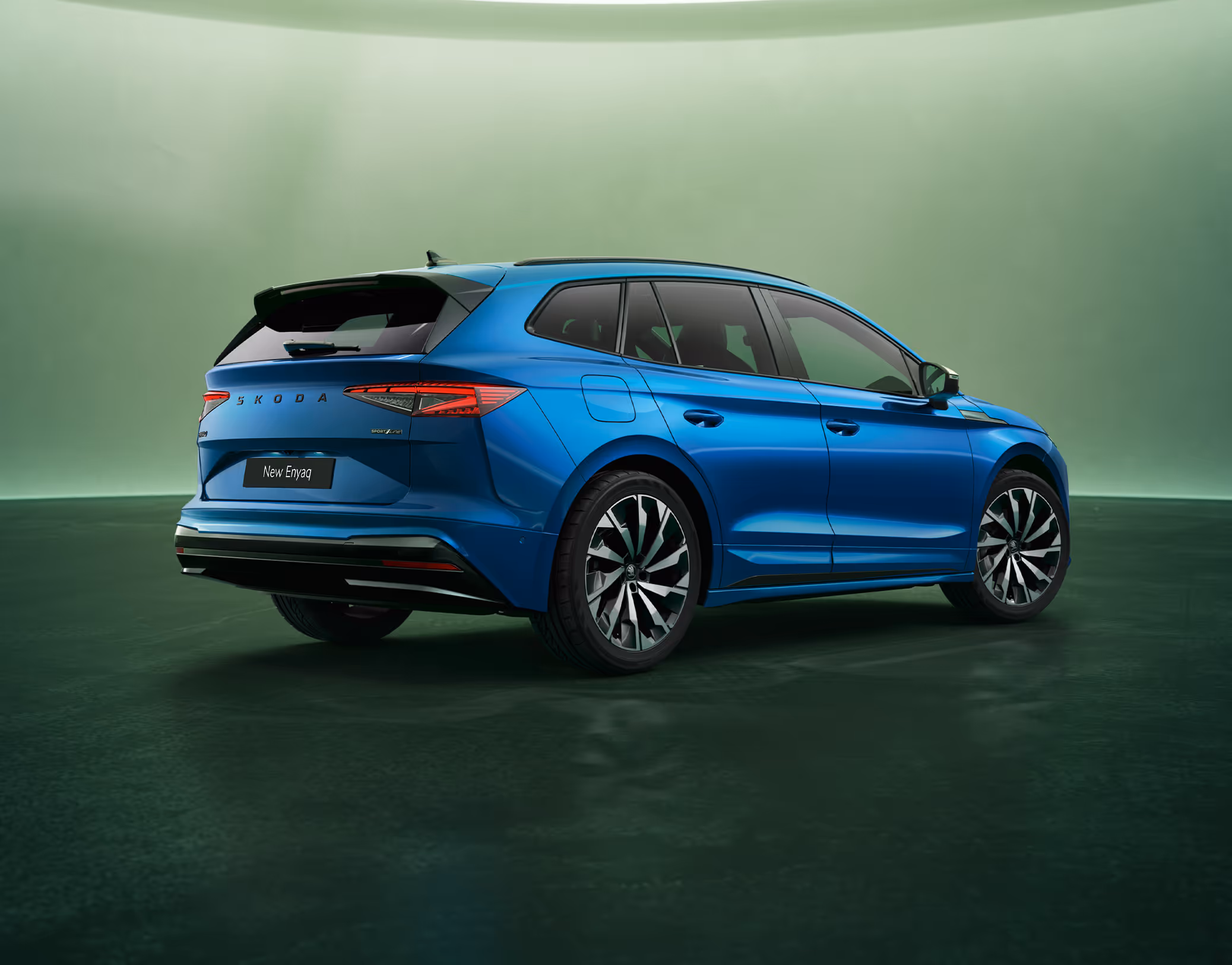 Schräge Heckansicht des Škoda Enyaq Sportline in der Farbe Race-Blau Metallic vor einem grünem Studiohintergrund. Die Rückleuchten und der prominente Škoda Schriftzug am Heck sind zu erkennen.