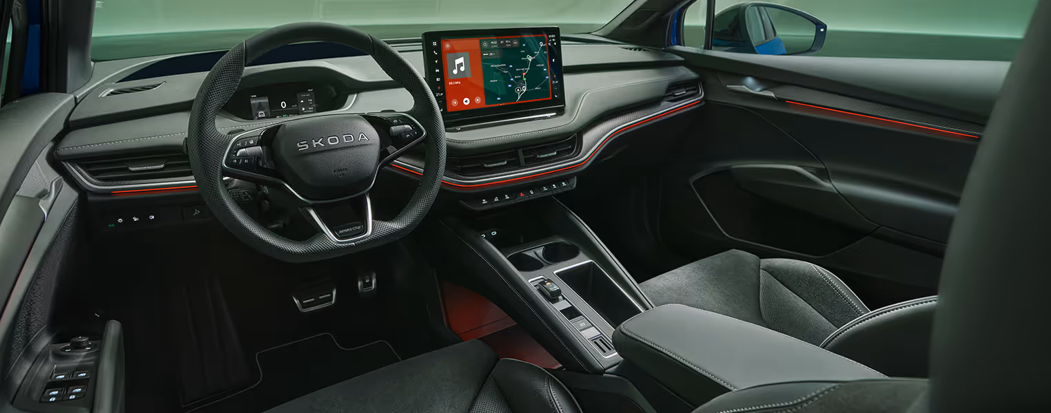 Blick aus der Fahrerperspektive in den sportlichen Innenraum des Škoda Enyaq in der Ausstattungslinie Sportline. Das schwarze Interieur mit Sportsitzen in Mikrofaser-Leder-Kombination wird durch rote Ambientebeleuchtung dynamisch in Szene gesetzt.