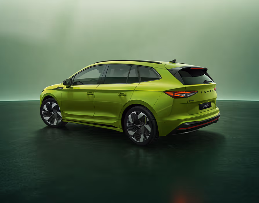 Ein Škoda Enyaq RS in der Lackierung Mamba-Grün in einer Dreiviertel-Heckansicht vor grünem Studiohintergrund. Das sportliche Design wird durch RS-spezifische Stoßfänger mit einem durchgehenden roten Reflektor, schwarze Designakzente und große, aerodynamisch optimierte Leichtmetallfelgen unterstrichen.