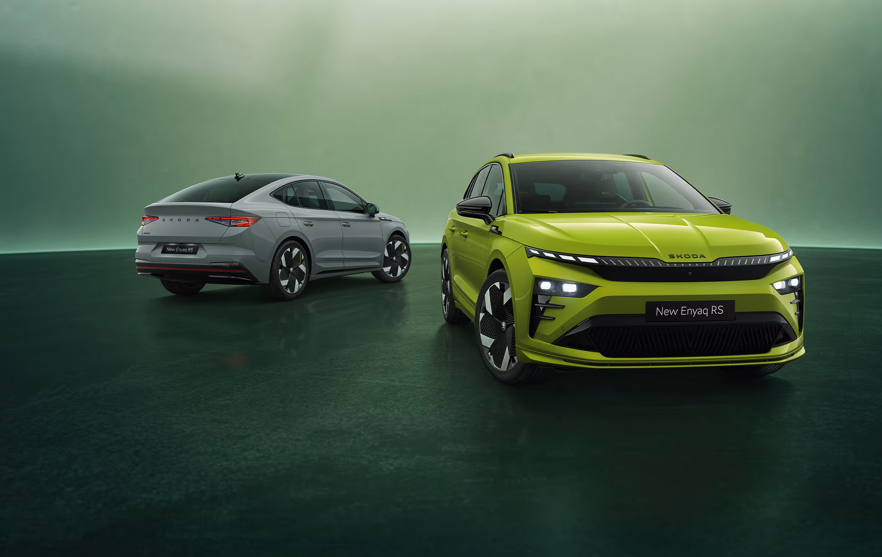 Grünes Studio-Setting. Im Vordergrund steht rechts der Škoda Enyaq RS als SUV-Variante in der Farbe Mamba-Grün in der Frontansicht. Dahinter befindet sich links das Enyaq Coupé RS in der Farbe Stahl-Grau mit seiner eleganten, abfallenden Dachlinie in der Heckansicht.