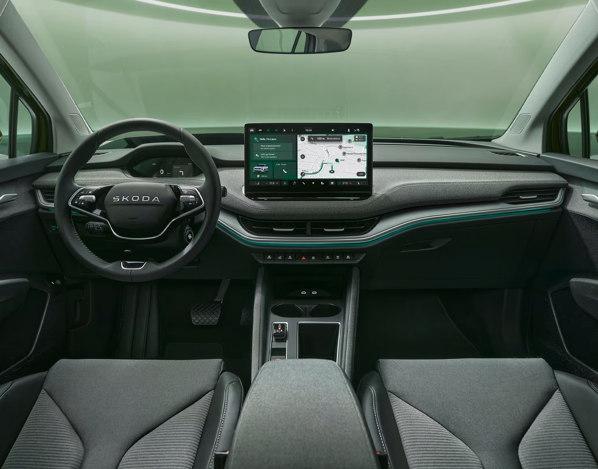 Eine symmetrische Weitwinkelaufnahme zeigt das Cockpit des Škoda Enyaq aus der Perspektive der Rücksitze. Das Interieur der Design Selection „Lodge“ zeichnet sich durch dunkle Materialien, eine durchgehende grüne Ambientebeleuchtung und das zentrale, freistehende 13-Zoll-Infotainmentdisplay aus.