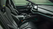 Ein Blick in den vorderen Innenraum des Škoda Enyaq RS mit Fokus auf den Fahrer- und Beifahrersitz. Das Interieur der Design Selection „RS Suite“ überzeugt durch perforierte schwarze Lederbezüge und Dekor in Carbon-Optik sowie grüne Ambientebeleuchtung.