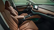 Ein Blick in den vorderen Innenraum des Škoda Enyaq mit Fokus auf den Fahrer- und Beifahrersitz. Die Sitze der Design Selection „ecoSuite“ sind mit cognacfarbenem Leder bezogen. Die grüne Ambientebeleuchtung leuchtet entlang des Armaturenbretts und der Fahrertür.