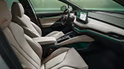 Ein Blick in den vorderen Innenraum des Škoda Enyaq mit Fokus auf den Fahrer- und Beifahrersitz. Die Sitze der Design Selection „L&K“ sind mit beigem Leder bezogen und weisen cognacfarbene Ziernähte auf. Die grüne Ambientebeleuchtung leuchtet entlang des Armaturenbretts und der Fahrertür.