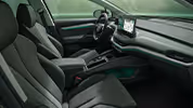 Ein Blick in den vorderen Innenraum des Škoda Enyaq mit Fokus auf den Fahrer- und Beifahrersitz. Das Interieur der Design Selection „Lodge“ ist mit dunklen Stoffen und einer grünen Ambientebeleuchtung ausgestattet, die das moderne Cockpit betont. Im Zentrum stehen das große, freistehende 13-Zoll-Infotainmentdisplay und das digitale Cockpit hinter dem Lenkrad.