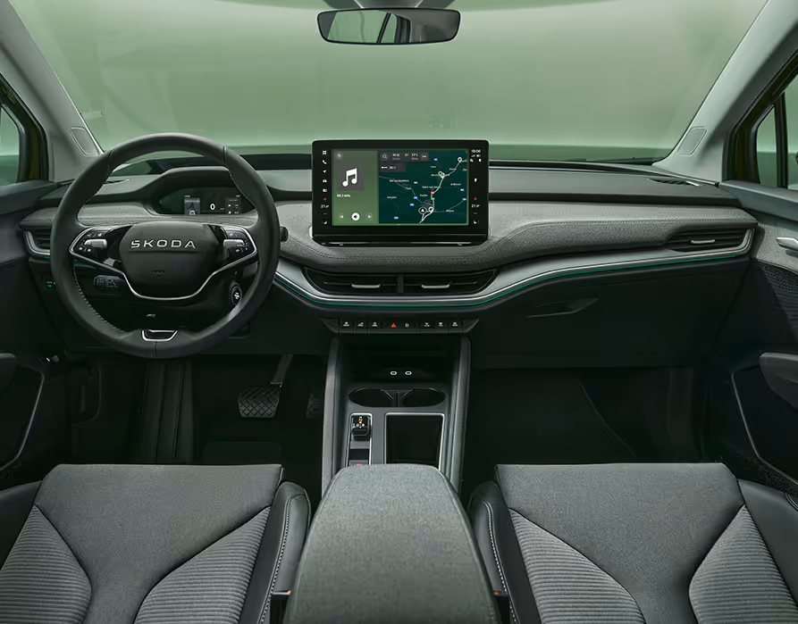 Eine symmetrische Weitwinkelaufnahme zeigt das Cockpit des Škoda Enyaq RS aus der Perspektive der Rücksitze. Das elegante Interieur der Design Selection „RS Lounge“ besticht durch perforierte schwarze Lederbezüge und Dekor in Carbon-Optik sowie grüne Ambientebeleuchtung.