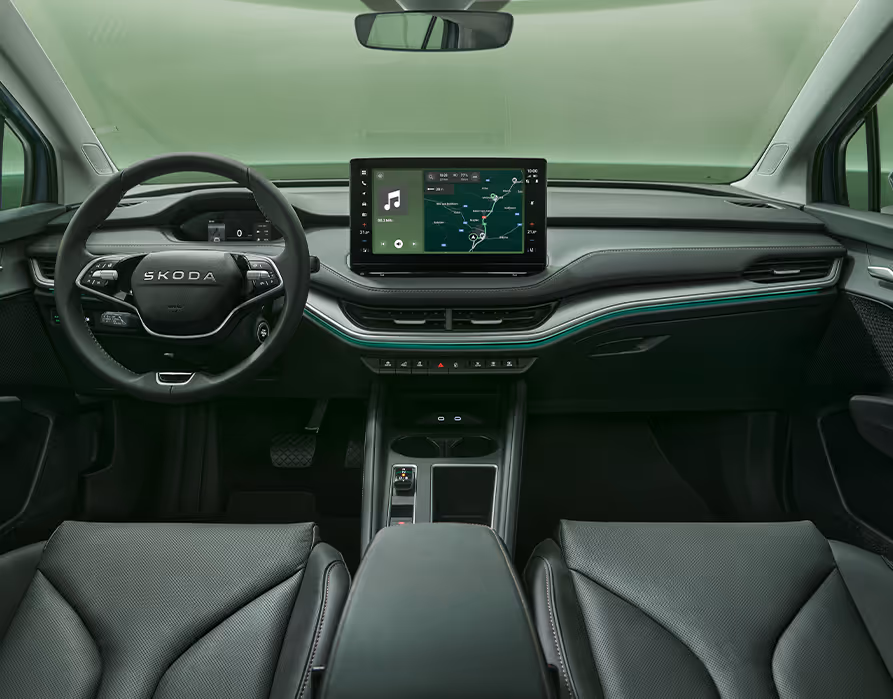 Blick über die Mittelarmlehne auf das Lenkrad, das Infotainmentsystem und das Armaturenbrett im Škoda Elroq. Türkise Ambient-Beleuchtung.