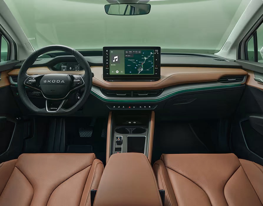 Blick über die Mittelarmlehne auf das Lenkrad, das Infotainmentsystem und das Armaturenbrett im Škoda Elroq. Türkise Ambient-Beleuchtung.