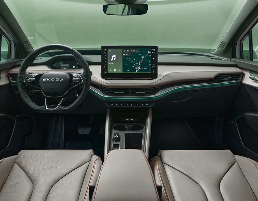 Blick über die Mittelarmlehne auf das Lenkrad, das Infotainmentsystem und das Armaturenbrett im Škoda Elroq. Türkise Ambient-Beleuchtung.