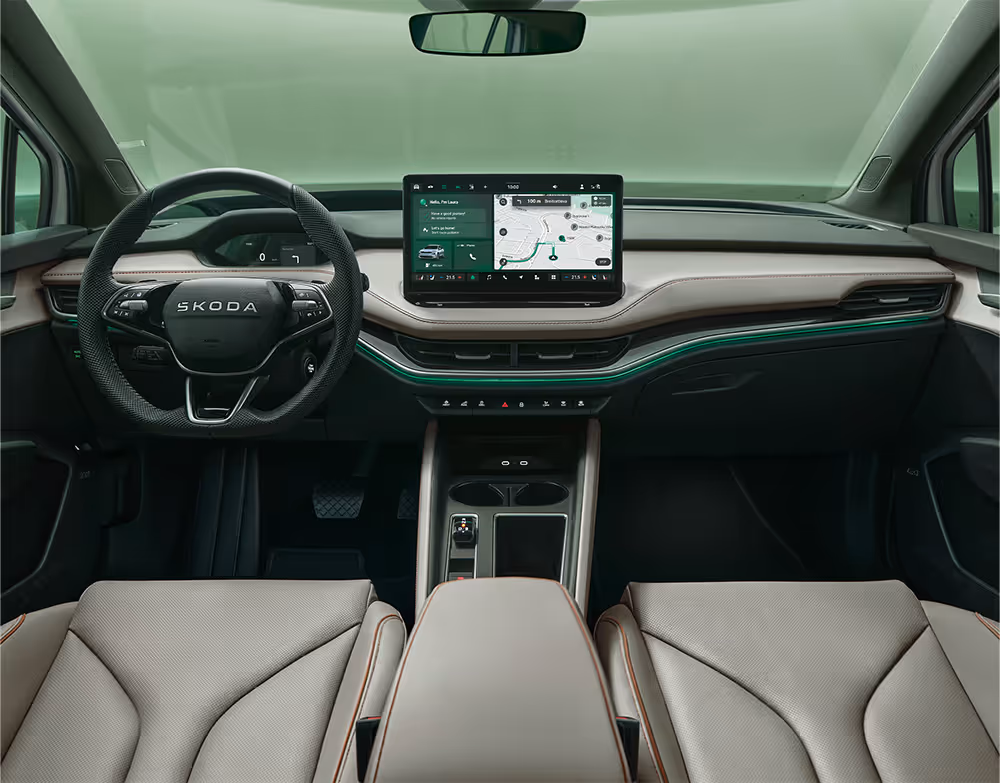 Blick über die Mittelarmlehne auf das Lenkrad, das Infotainmentsystem und das Armaturenbrett im Škoda Elroq. Türkise Ambient-Beleuchtung.