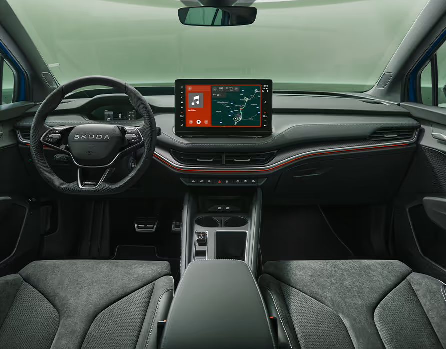 Eine symmetrische Weitwinkelaufnahme zeigt das Cockpit des Škoda Enyaq Sportline aus der Perspektive der Rücksitze. Das elegante Interieur der Design Selection „Sportline“ besticht durch perforierte schwarze Lederbezüge und Dekor in Carbon-Optik sowie rote Ambientebeleuchtung.