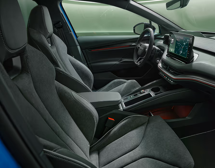 Ein Blick in den vorderen Innenraum des Škoda Enyaq RS mit Fokus auf den Fahrer- und Beifahrersitz. Das schwarze Interieur der Design Selection "Sportline" mit Sportsitzen in Mikrofaser-Leder-Kombination wird durch rote Ambientebeleuchtung dynamisch in Szene gesetzt.