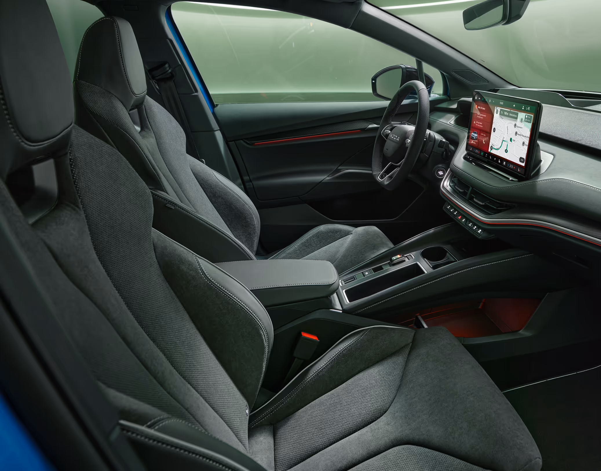 Ein Blick in den vorderen Innenraum des Škoda Enyaq RS mit Fokus auf den Fahrer- und Beifahrersitz. Das schwarze Interieur der Design Selection "Sportline" mit Sportsitzen in Mikrofaser-Leder-Kombination wird durch rote Ambientebeleuchtung dynamisch in Szene gesetzt.