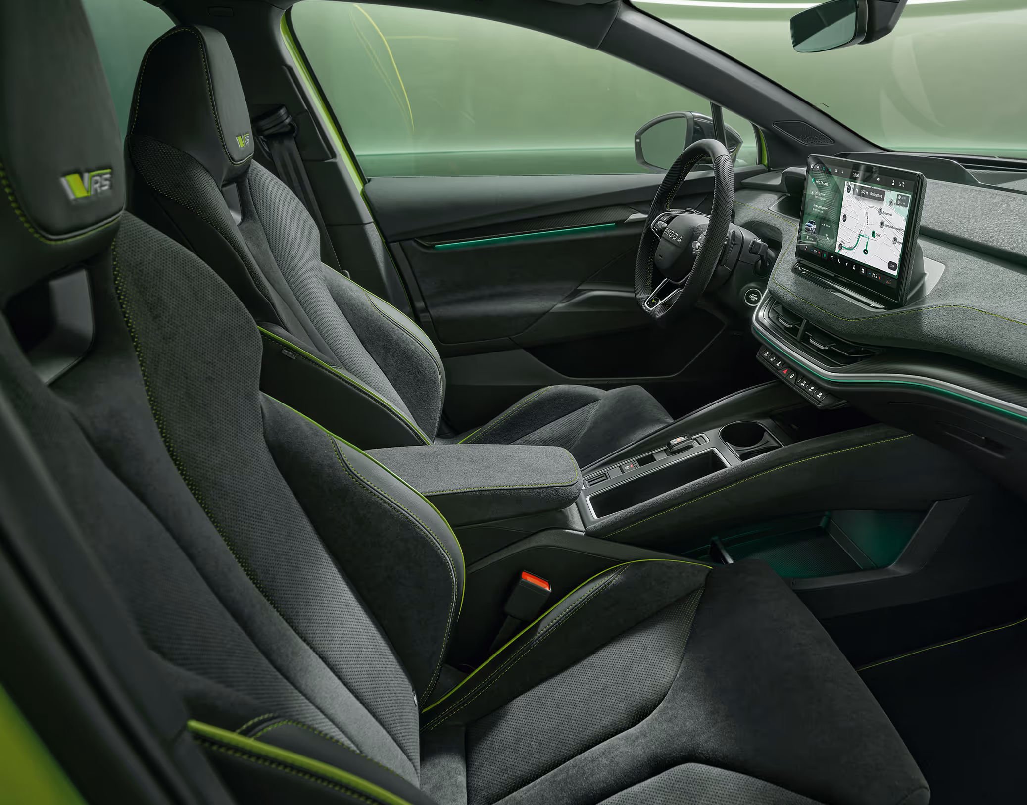 Ein Blick in den vorderen Innenraum des Škoda Enyaq RS mit Fokus auf den Fahrer- und Beifahrersitz. Das Interieur der Design Selection „RS Lounge“ überzeugt durch perforierte schwarze Lederbezüge und Dekor in Carbon-Optik sowie grüne Ambientebeleuchtung.
