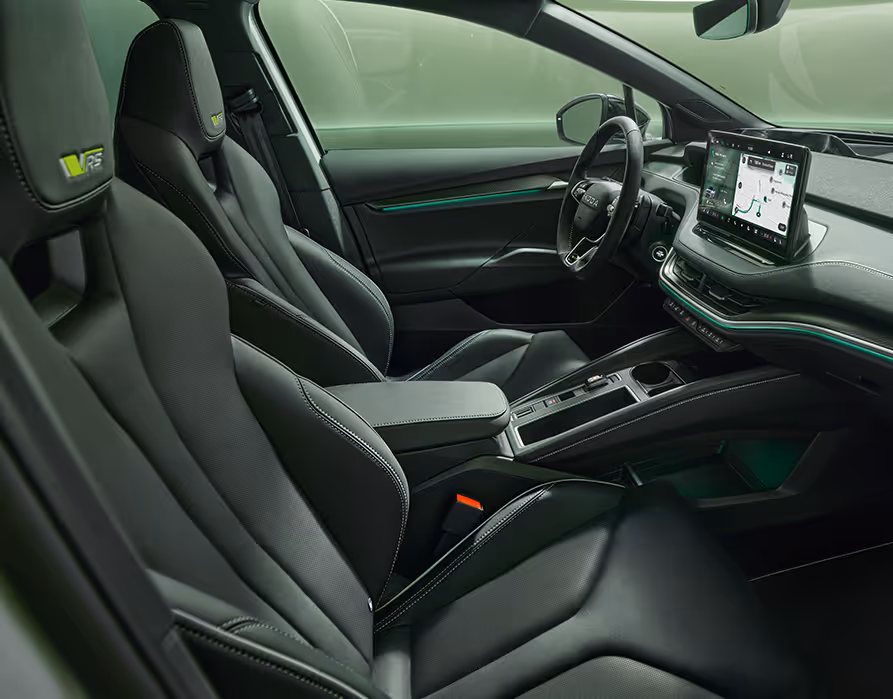 Ein Blick in den vorderen Innenraum des Škoda Enyaq RS mit Fokus auf den Fahrer- und Beifahrersitz. Das Interieur der Design Selection „RS Suite“ überzeugt durch perforierte schwarze Lederbezüge und Dekor in Carbon-Optik sowie grüne Ambientebeleuchtung.