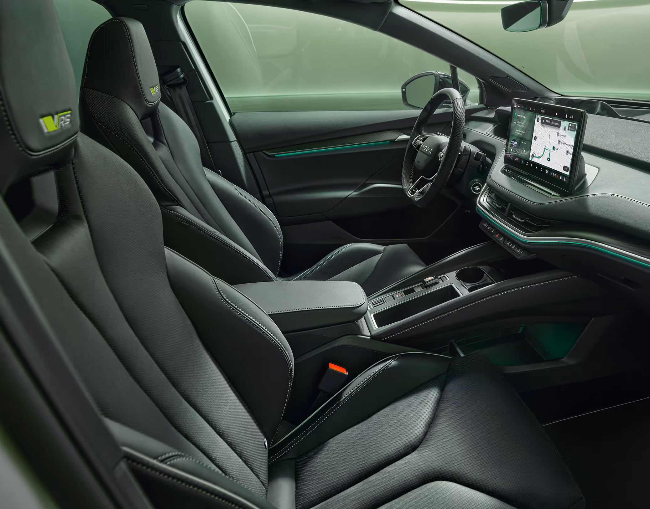 Ein Blick in den vorderen Innenraum des Škoda Enyaq RS mit Fokus auf den Fahrer- und Beifahrersitz. Das Interieur der Design Selection „RS Suite“ überzeugt durch perforierte schwarze Lederbezüge und Dekor in Carbon-Optik sowie grüne Ambientebeleuchtung.