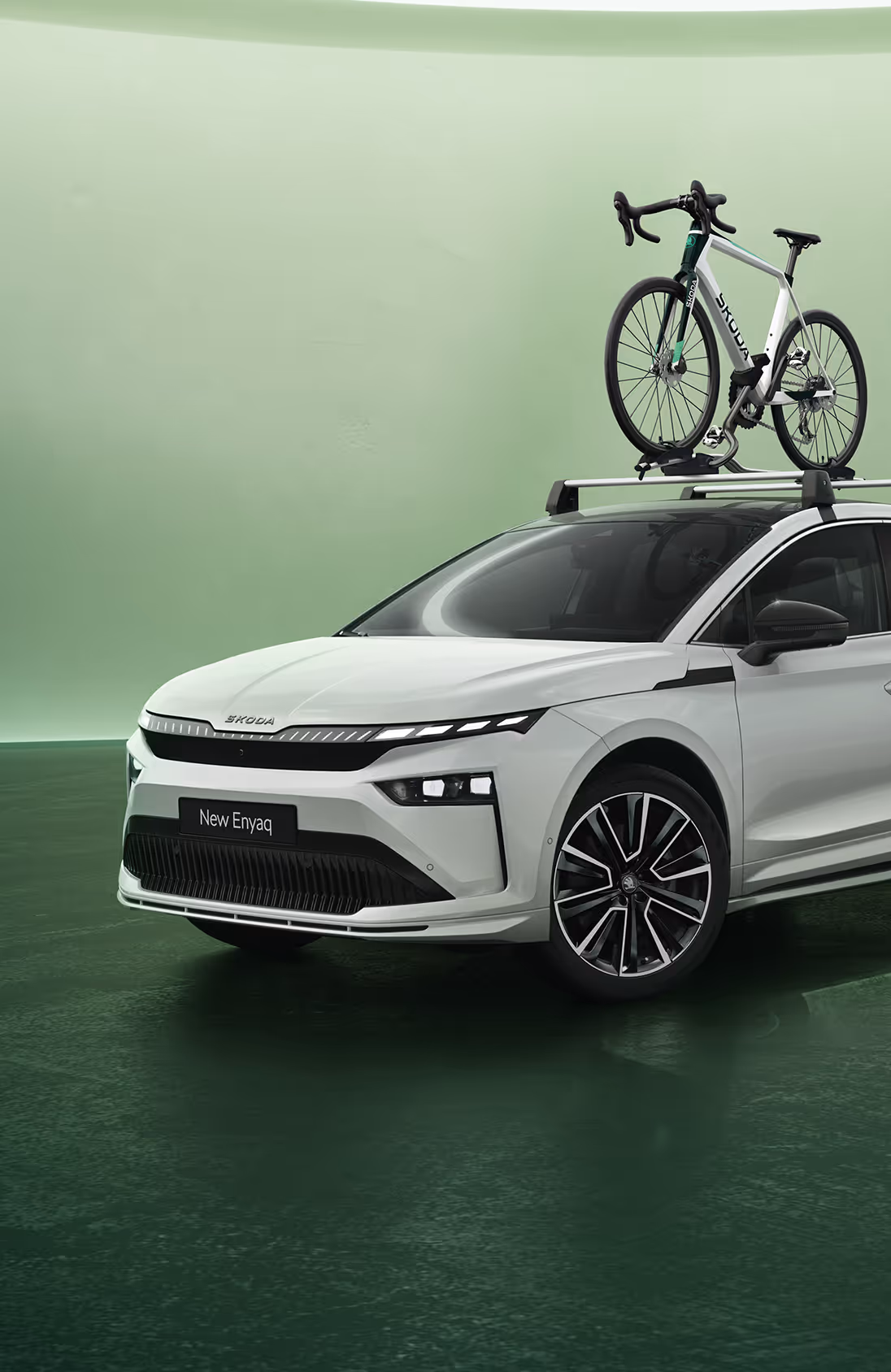 Frontalansicht eines Škoda Elroq mit einer Dachbox vor grünem Studiohintergrund. Das Fahrzeug ist für eine Reise mit zusätzlichem Gepäck ausgestattet.