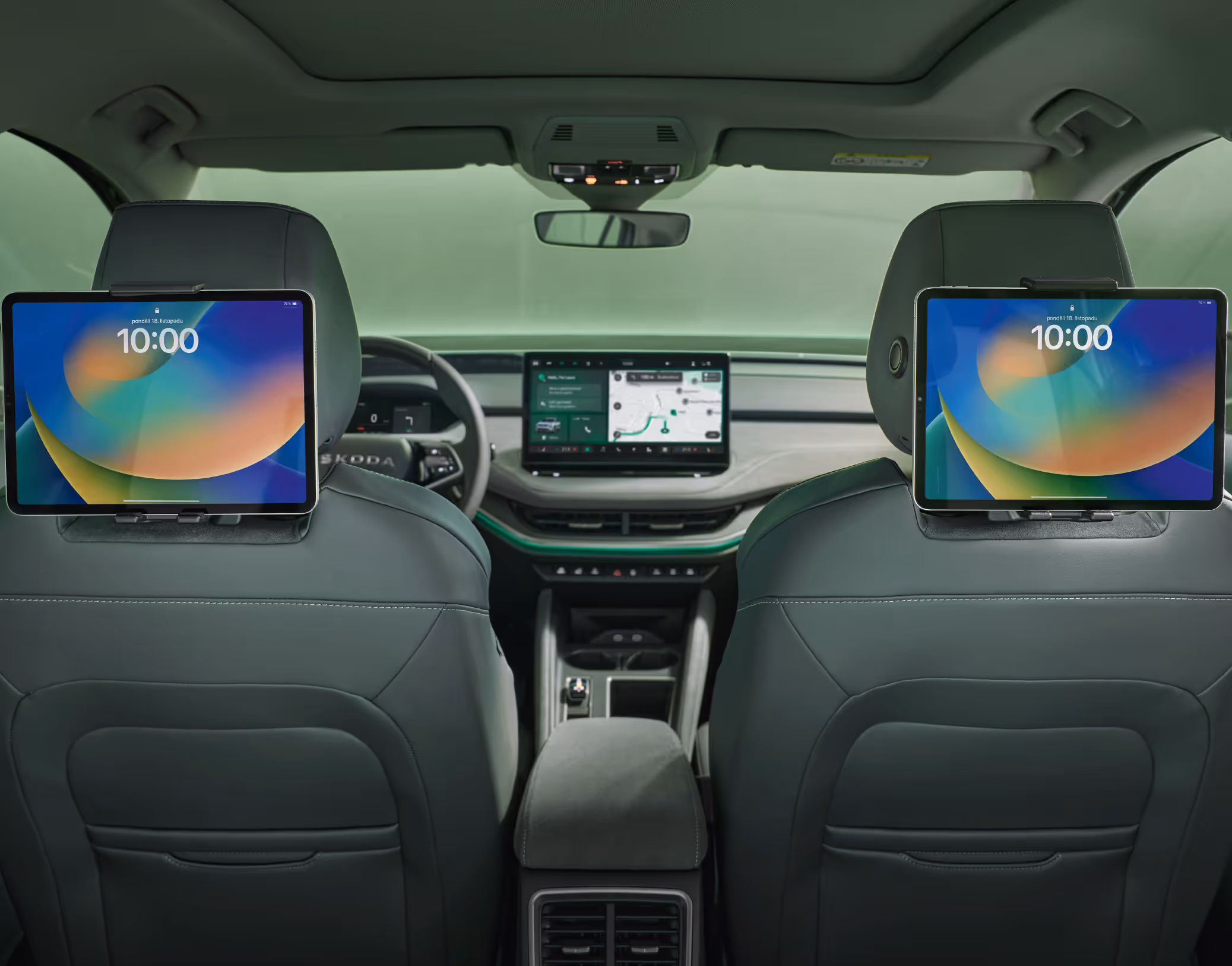 Blick von der Rückbank eines Škoda Enyaq nach vorn in das Cockpit, das in der Design Selection Loft gehalten ist. An den Kopfstützen der Vordersitze sind zwei Multimediahalter befestigt, in denen jeweils ein Tablet steckt. Im Hintergrund sind das Armaturenbrett mit dem zentralen Infotainment-Display und das Lenkrad zu sehen.