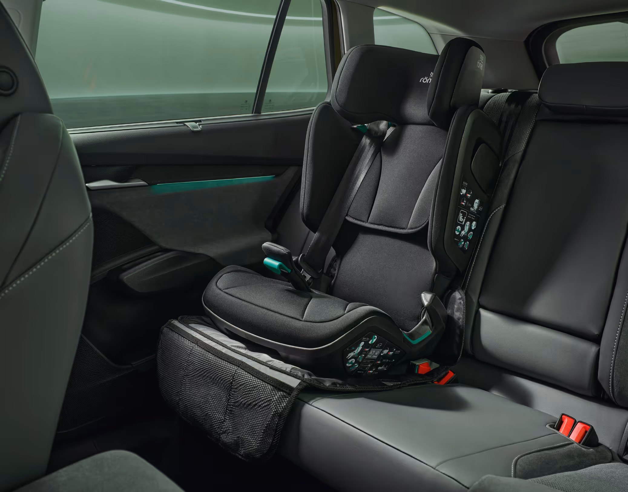 Blick auf die Rückbank eines Škoda Enyaq in der Design Selection "Loft". Auf dem rechten Sitzplatz ist ein schwarzer Kleinkind-Kindersitz auf einer Schutzunterlage befestigt. Die Aufnahme erfasst den Bereich vom Beifahrersitz bis zur hinteren Seitentür und zeigt die Platzverhältnisse im Innenraum.