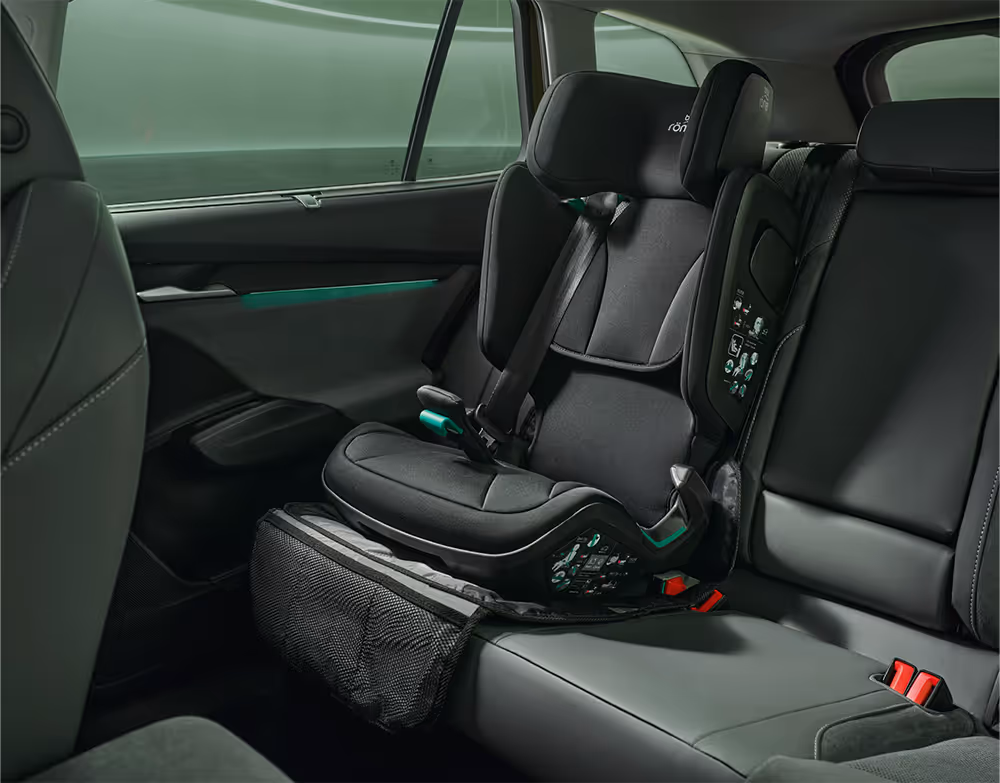 Blick auf die Rückbank eines Škoda Enyaq in der Design Selection "Loft". Auf dem rechten Sitzplatz ist ein schwarzer Kleinkind-Kindersitz auf einer Schutzunterlage befestigt. Die Aufnahme erfasst den Bereich vom Beifahrersitz bis zur hinteren Seitentür und zeigt die Platzverhältnisse im Innenraum.