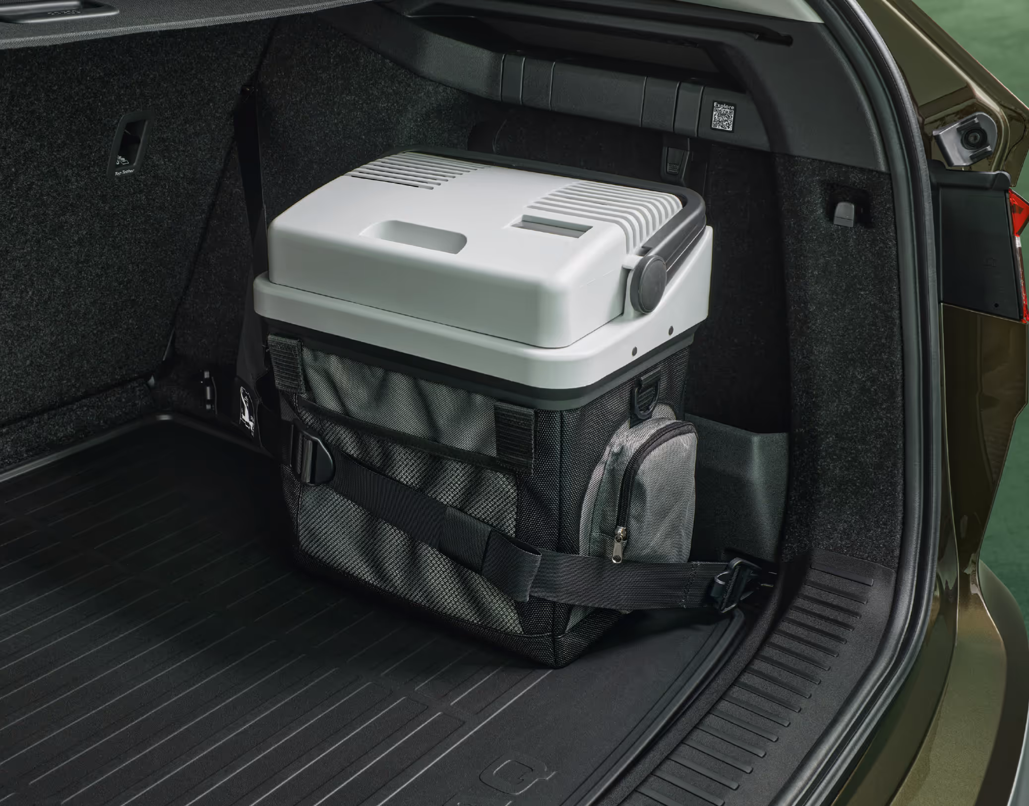 Eine Detailansicht der rechten Kofferraumhälfte eines Škoda Enyaq. Auf der Kunststoff-Kofferraumwanne steht an der Kofferraumwand eine große, tragbare thermoelektrische Kühlbox, die mit einem schwarzen Gurt gesichert ist.