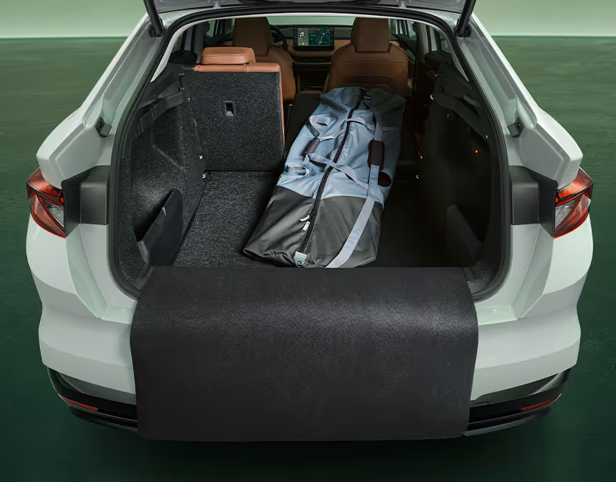 Der geöffnete Kofferraum eines Škoda Enyaq Coupé in der Farbe Moon-Weiß Perleffekt mit umgeklapptem Rücksitz. Im vergrößerten Laderaum liegt eine lange Tasche, und eine schwarze Schutzmatte ist über die Ladekante und den Stoßfänger ausgeklappt.