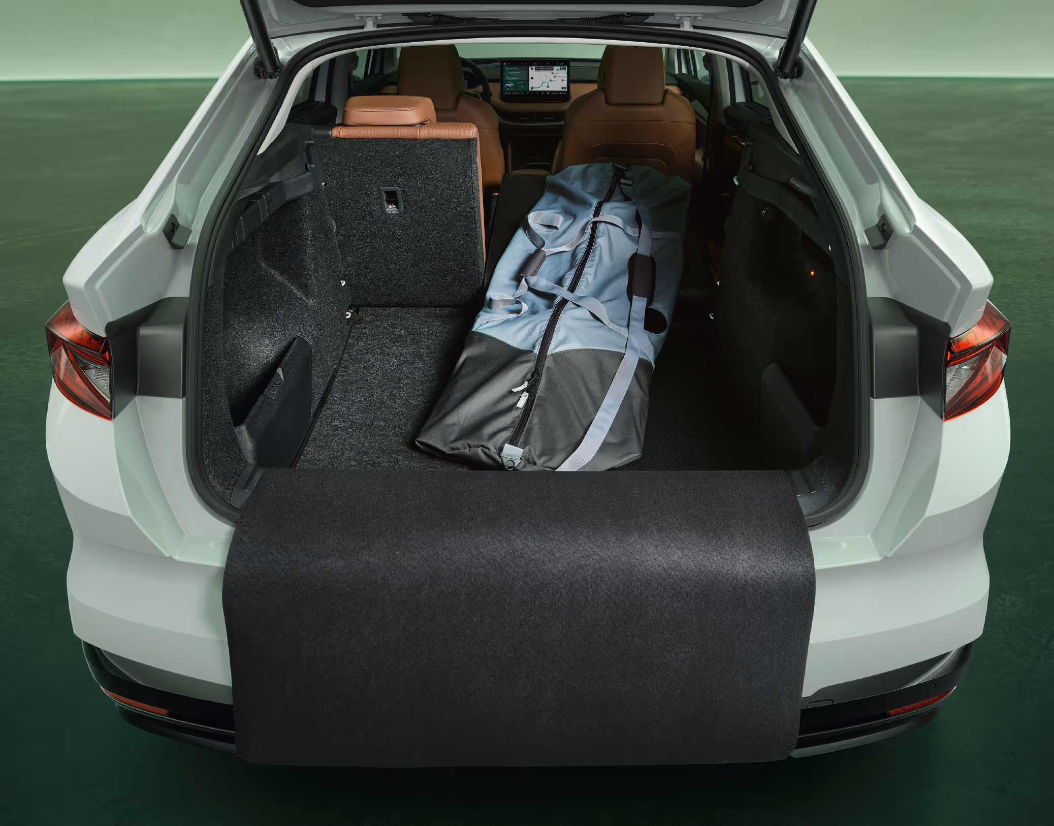 Der geöffnete Kofferraum eines Škoda Enyaq Coupé in der Farbe Moon-Weiß Perleffekt mit umgeklapptem Rücksitz. Im vergrößerten Laderaum liegt eine lange Tasche, und eine schwarze Schutzmatte ist über die Ladekante und den Stoßfänger ausgeklappt.