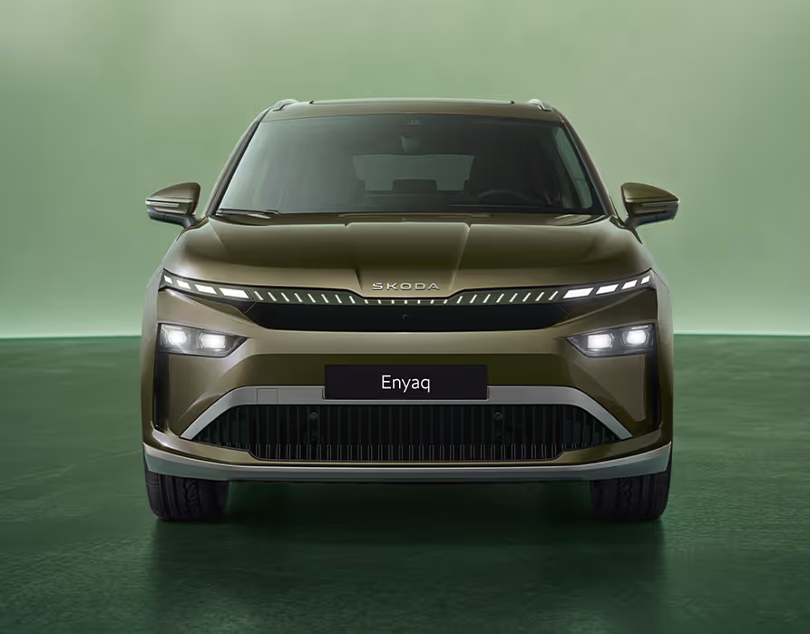 Frontalansicht des Škoda Enyaq in der Farbe Olibo-Grün Metallic vor einem grünen Studiohintergrund. Das neue Tech-Deck-Face des Fahrzeugs betont das moderne Design der Frontpartie.