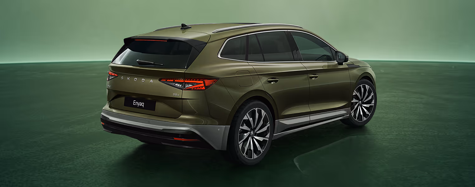 Schräge Heckansicht des Škoda Enyaq in der Farbe Olibo-Grün Metallic vor einem grünem Studiohintergrund. Die Rückleuchten und der prominente Škoda Schriftzug am Heck sind zu erkennen.