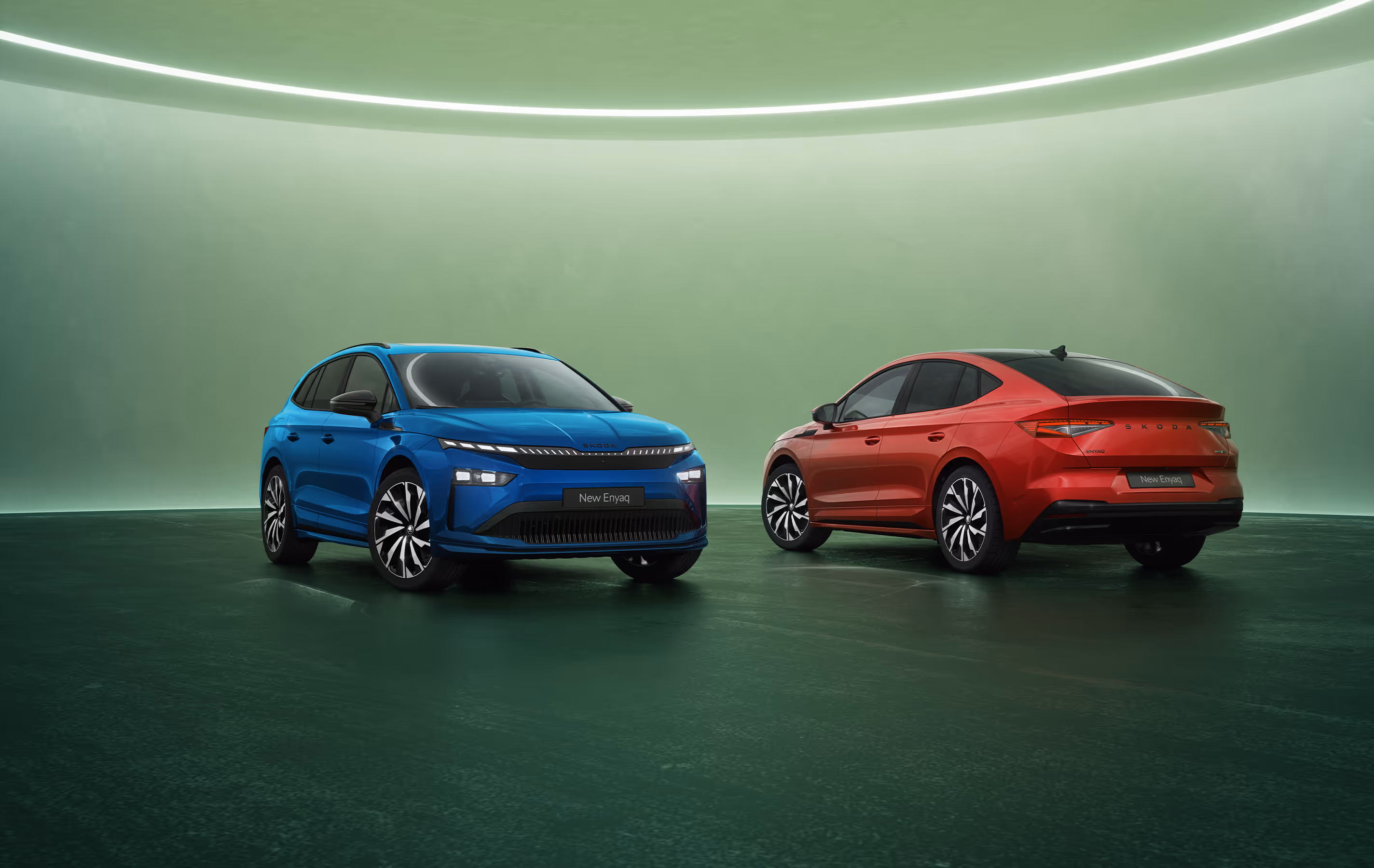Zwei Škoda Enyaq Modelle der Sportline-Ausstattungslinie vor grünen Studiohintergrund. Links steht ein Enyaq in der SUV-Variante in der Farbe Race-Blau Metallic mit Frontansicht, rechts ist ein Enyaq Coupé in der Farbe Velvet-Rot Premium Metallic mit abfallender Dachlinie in der Heckansicht zu sehen.
