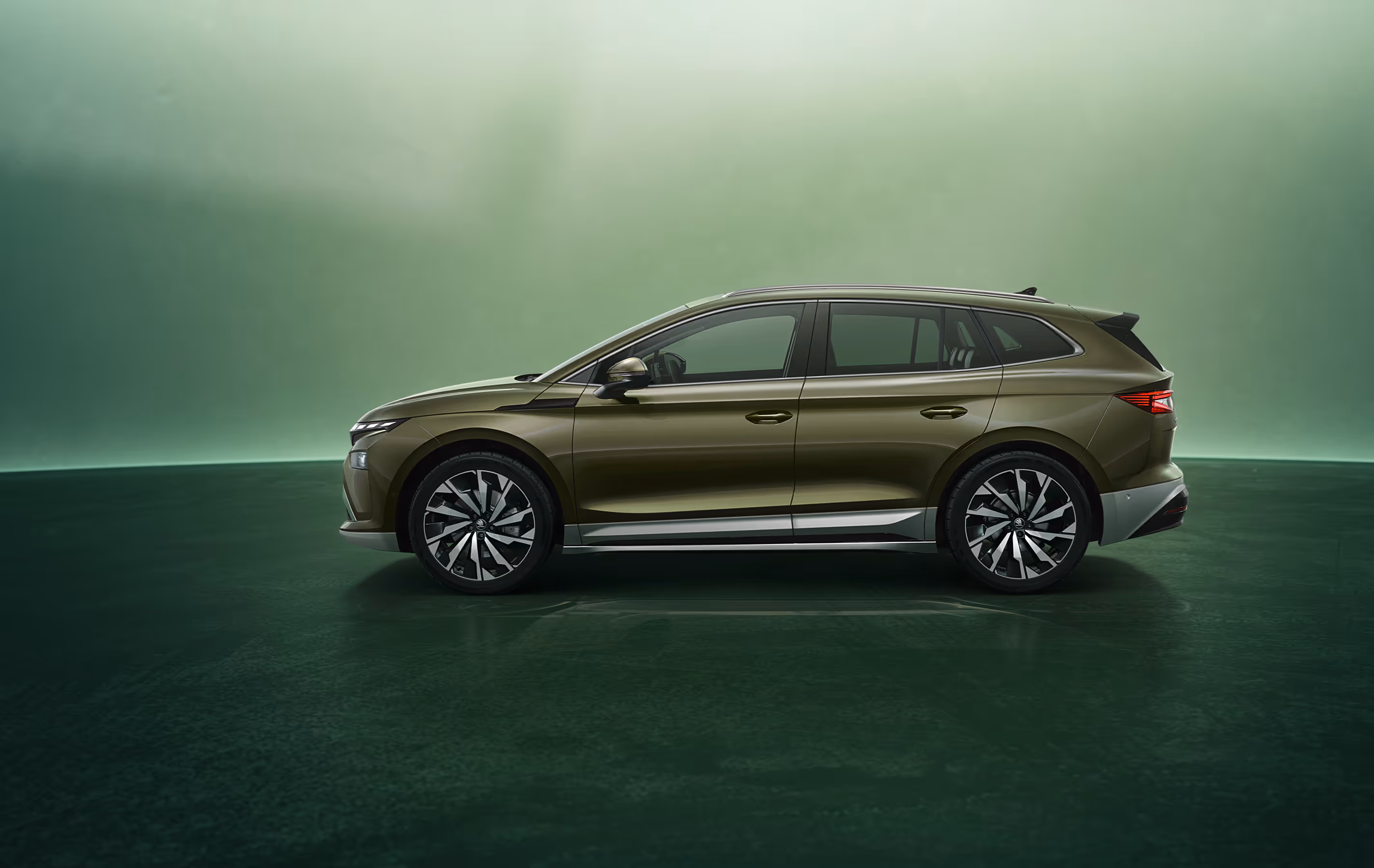 Seitenansicht des Škoda Enyaq in der Farbe Olibo-Grün Metallic vor einem grünen Studiohintergrund. Das Fahrzeug zeigt seine klare Linienführung, die robusten Radkästen und die aerodynamische Silhouette.