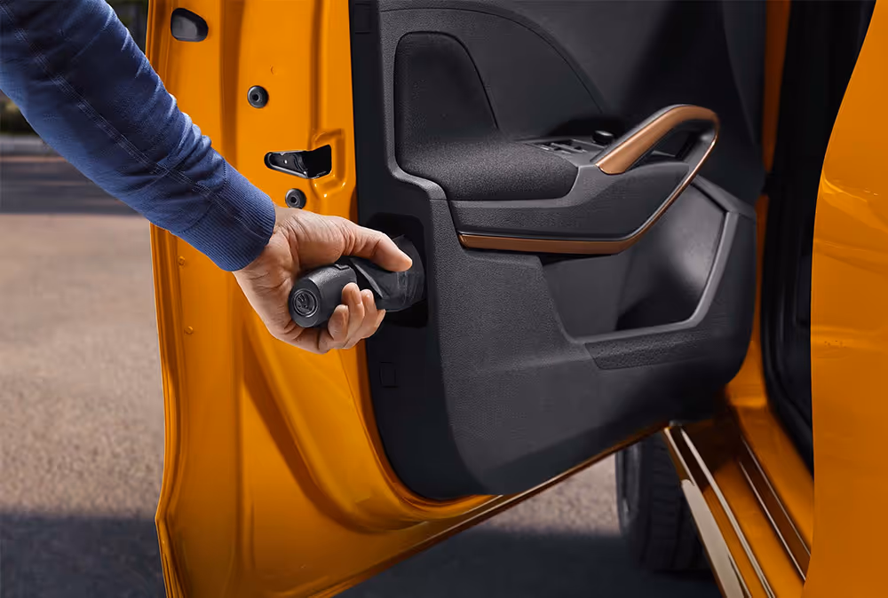 Detailansicht der geöffneten Tür eines Škoda Fabia in Phoenix-Orange Metallic, bei der eine Hand einen Regenschirm aus dem integrierten Ablagefach in der Türverkleidung zieht. Dieses praktische „Simply Clever“-Feature ermöglicht das griffbereite Verstauen eines Regenschirms direkt im Fahrzeug. Akzente setzt zudem der Türzuziehgriff in der Farbe Copper, der sich harmonisch in die dunkle Innenverkleidung einfügt.