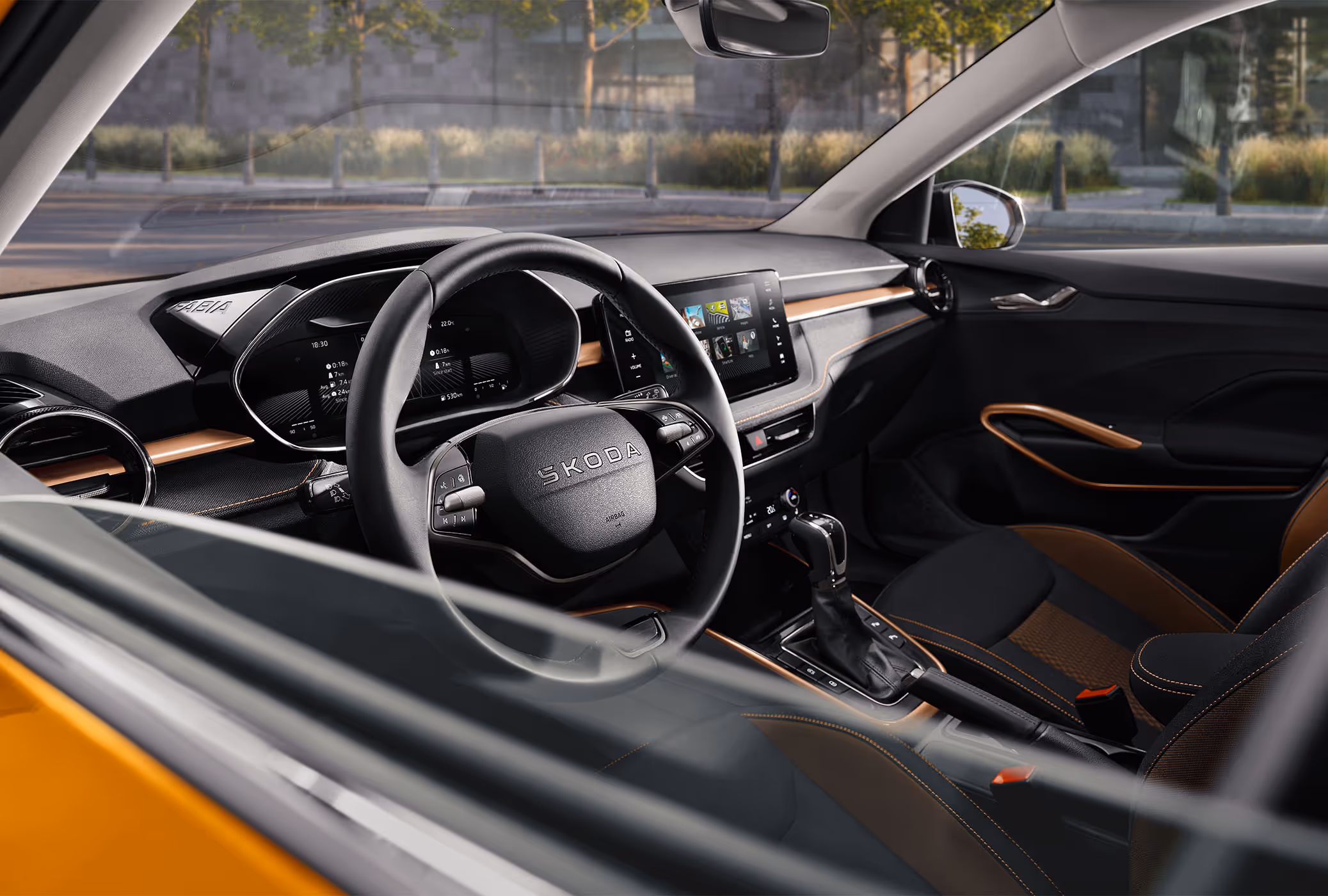Wir blicken durch das geöffnete Fenster der Fahrertür auf das 2-Speichen-Multifunktionslenkrad im Škoda Fabia, das mittig den Markenschriftzug sowie diverse Bedienelemente trägt. Dahinter zeigt das digitale Virtual Cockpit Fahrdaten wie Reichweite und Verbrauch an. Rechts daneben ist das Infotainment-Display mit seiner Kachel-Struktur für Medien und Fahrzeugeinstellungen zu sehen.