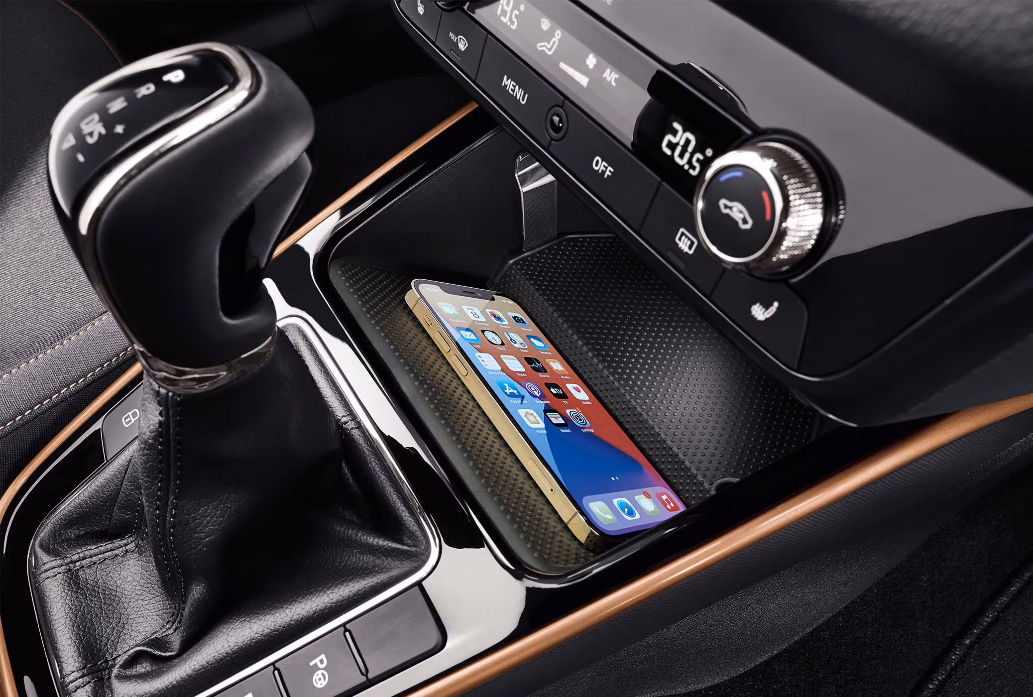 Ein Smartphone liegt in der Phonebox der Mittelkonsole, die das induktive Aufladen von Mobiltelefonen ermöglicht. Direkt daneben befindet sich der Wählhebel des DSG-Getriebes, umrahmt von einer kupferfarbenen Zierleiste. Oberhalb der Ablage ist die Bedieneinheit der Climatronic mit ihrer digitalen Temperaturanzeige und den Drehreglern platziert.