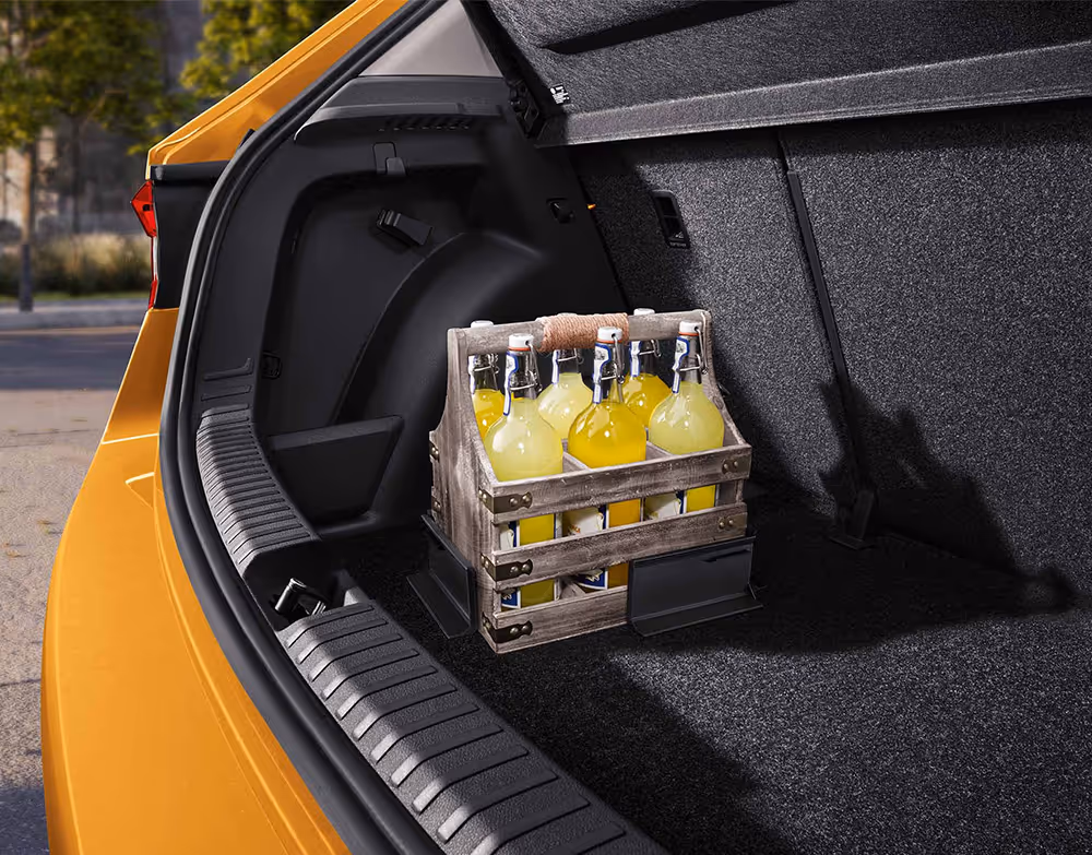 Ein hölzerner Flaschenträger steht auf dem Kofferraumboden des Škoda Fabia und wird durch zwei flexible Cargo-Elemente sicher an seinem Platz gehalten. Die L-förmigen Kunststoffwinkel haften mittels Klettverschluss am Boden des Laderaums und verhindern ein Verrutschen der Ladung während der Fahrt. Links begrenzen die schwarze Ladekante und die Karosserie in Phoenix-Orange Metallic den Bildausschnitt.