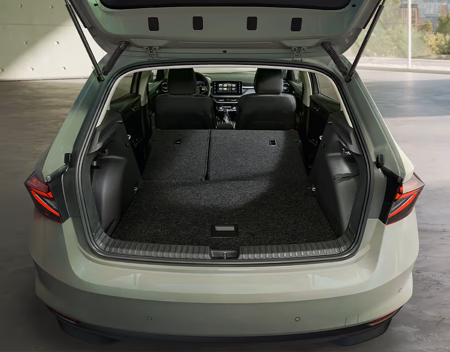 Eine Ansicht von hinten in den geöffneten Kofferraum des Škoda Fabia zeigt die vollständig umgeklappten Rücksitzlehnen. Die so entstandene, mit dunklem Stoff bezogene Ladefläche reicht bis an die Rückenlehnen der Vordersitze heran. Durch den Innenraum hindurch ist der Blick auf das Cockpit und das zentrale Infotainment-Display frei.