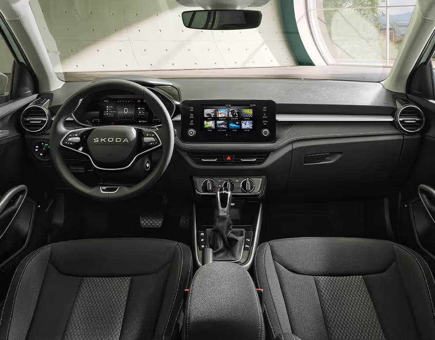 Ein Blick in den Innenraum des Škoda Fabia der Ausstattungslinie Selection zeigt die Design Selection Lodge mit ihren warmen Farbakzenten. Die Sitzbezüge und das stoffbezogene Dekorelement am Armaturenbrett zeichnen sich durch kupferfarbene Ziernähte und Details aus. Ergänzt wird das Interieur durch ein zweispeichiges Multifunktionslenkrad, ein freistehendes Infotainment-Display und den Wählhebel des Automatikgetriebes.