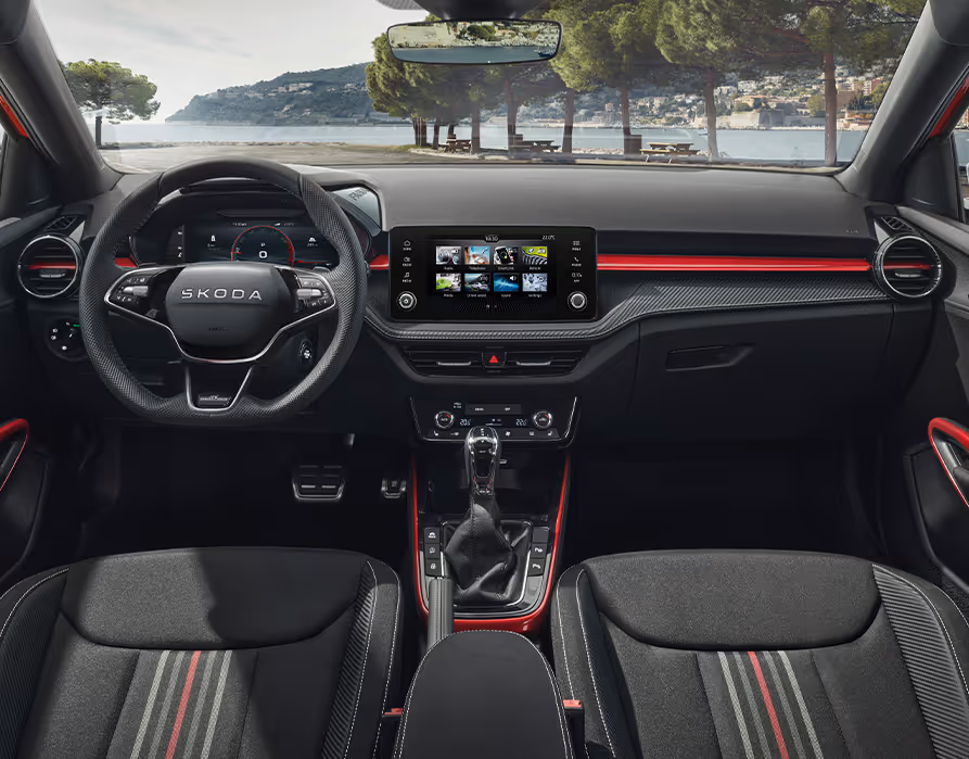 Ein Blick in den Innenraum des Škoda Fabia der Ausstattungslinie Selection zeigt die Design Selection Monte Carlo mit ihren markanten roten Akzenten an Armaturenbrett, Mittelkonsole und Türgriffen. Das Cockpit wird durch ein perforiertes Dreispeichen-Sportlenkrad, Dekorelemente in Carbon-Optik sowie Edelstahlpedale geprägt. Die schwarzen Sportsitze mit spezifischem Streifendesign unterstreichen den dynamischen Charakter des Interieurs.