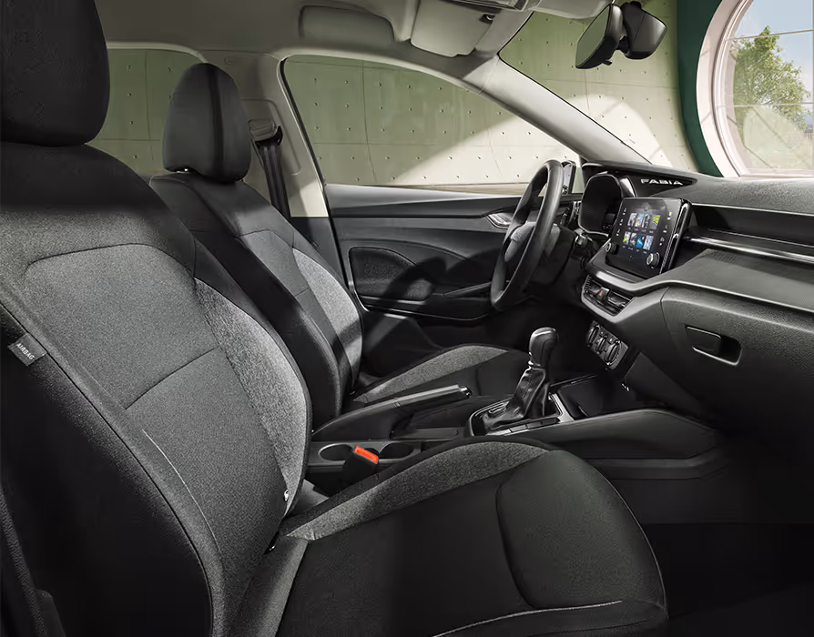 Eine Seitenansicht der Vordersitze zeigt das funktionale Interieur der Design Selection Studio mit Sitzbezügen in Schwarz und Grau. Das Armaturenbrett verfügt über eine genarbte Dekorleiste und ein schlichtes zweispeichiges Lenkrad vor dem Kombiinstrument. Die Mittelkonsole ist mit einer manuellen Handbremse und offenen Ablagemöglichkeiten ausgestattet.
