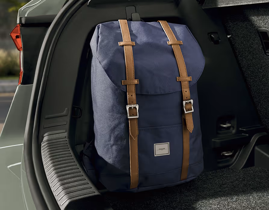 Eine Detailaufnahme im Kofferraum zeigt einen stabilen Haken an der Seitenverkleidung, an dem ein blauer Rucksack mit braunen Riemen aufgehängt ist. Der Rucksack hängt dadurch aufrecht im seitlichen Bereich des Laderaums, unmittelbar neben der geriffelten Kunststoffverkleidung der Ladekante.