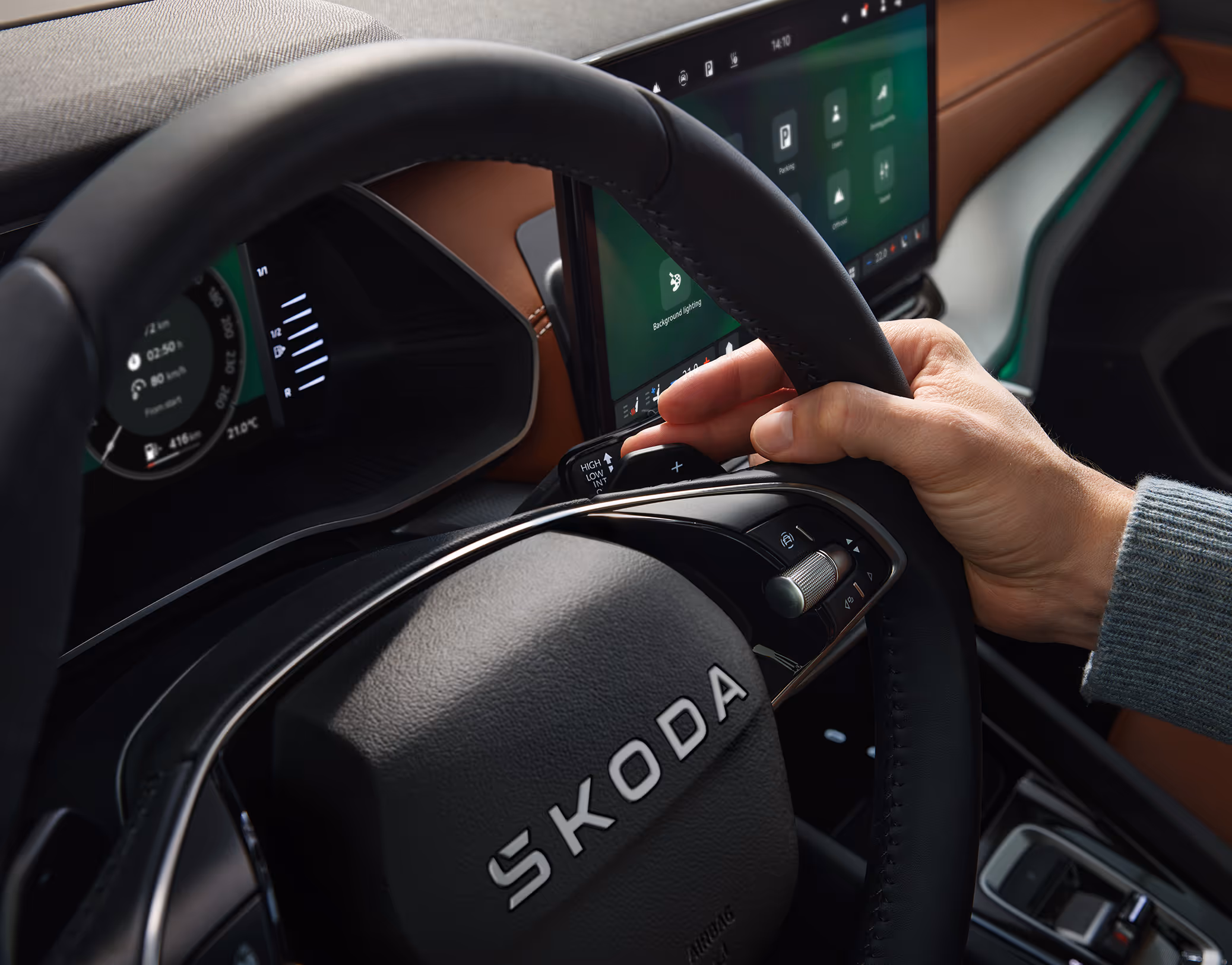 Eine Nahaufnahme zeigt die Hand eines Fahrers, die den Bedienhebel für den Adaptiven Abstandsassistenten (ACC) am Lenkrad eines Škoda Octavia betätigt. Die Aufnahme fokussiert auf die Interaktion mit den Bedienelementen, während im Hintergrund das digitale Cockpit und das cognac-farbene Armaturenbrett der Design Selection Suite zu sehen sind.