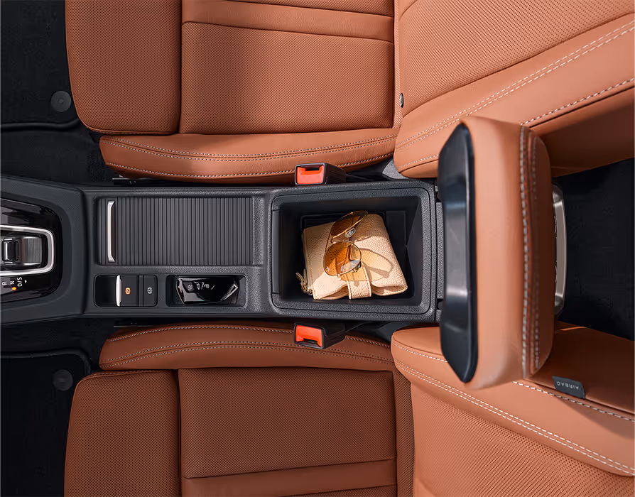 Eine Draufsicht der Mittelkonsole eines Škoda Octavia zeigt die verschiedenen Ablagemöglichkeiten zwischen den beiden Vordersitzen der Design Selection Suite in Cognac. Ein Fach beherbergt den Autoschlüssel, während ein größeres ein Portemonnaie und eine Sonnenbrille enthält. Links im Bild ist der DSG-Wählhebel zu sehen.