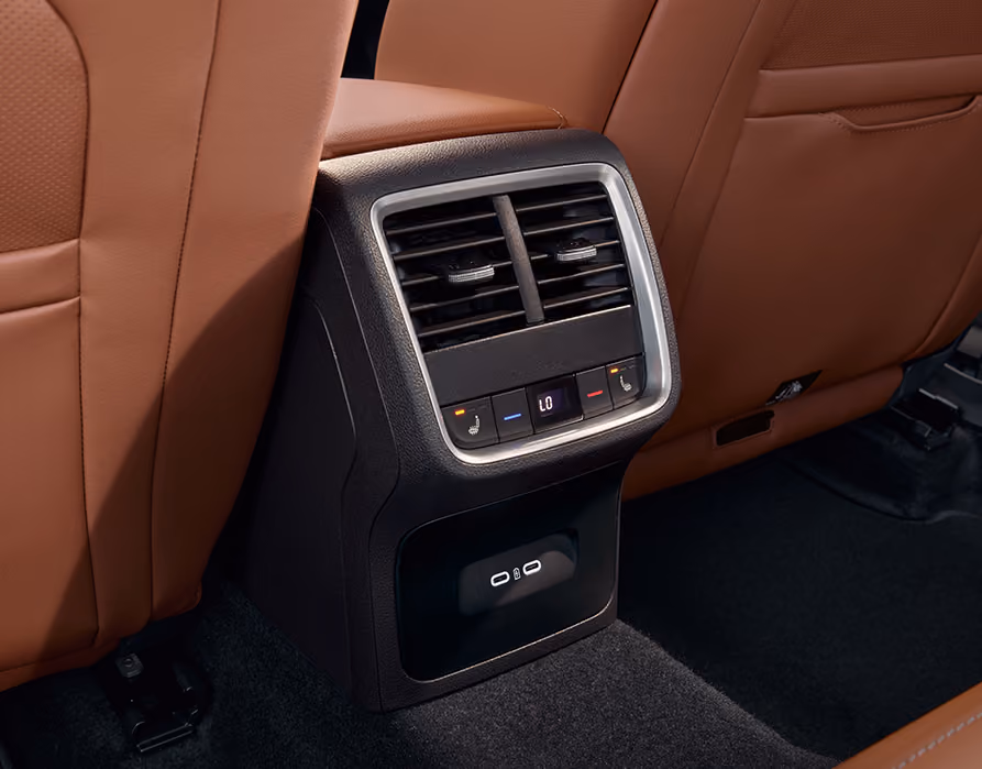Eine Nahaufnahme zeigt die Rückseite der Mittelkonsole eines Škoda Octavia. Umgeben von den cognac-farbenen Ledersitzen der Design Selection Suite, sind die Lüftungsdüsen, die Bedienelemente für die hintere Klimatisierung und Sitzheizung sowie zwei USB-C-Anschlüsse zu sehen. Der Fußraum wird von einer grünen Ambientebeleuchtung erhellt.