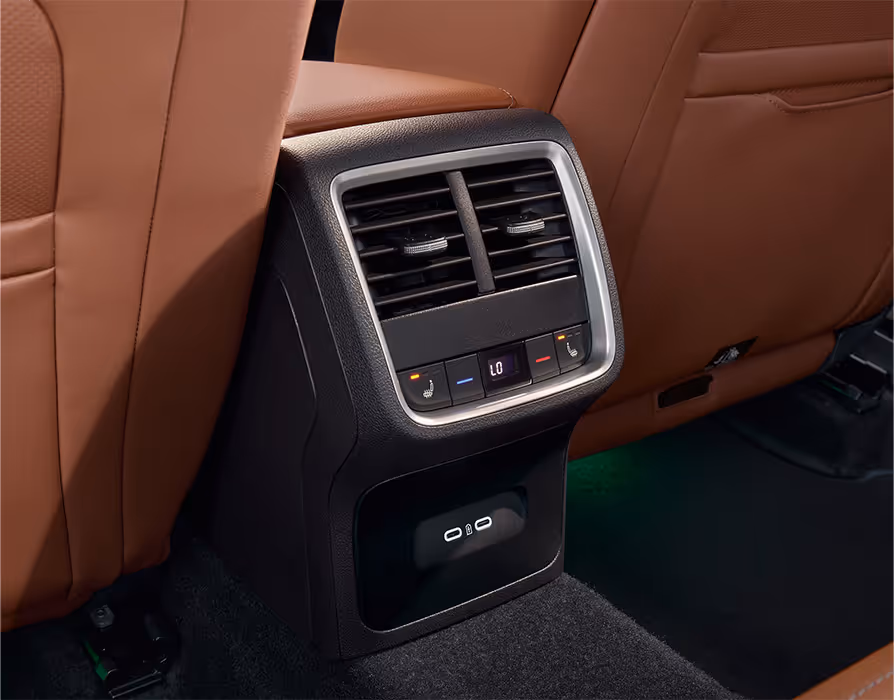 Eine Nahaufnahme zeigt die Rückseite der Mittelkonsole eines Škoda Octavia. Umgeben von den cognac-farbenen Ledersitzen der Design Selection Suite, sind die Lüftungsdüsen, die Bedienelemente für die hintere Klimatisierung und Sitzheizung sowie zwei USB-C-Anschlüsse zu sehen. Der Fußraum wird von einer grünen Ambientebeleuchtung erhellt.