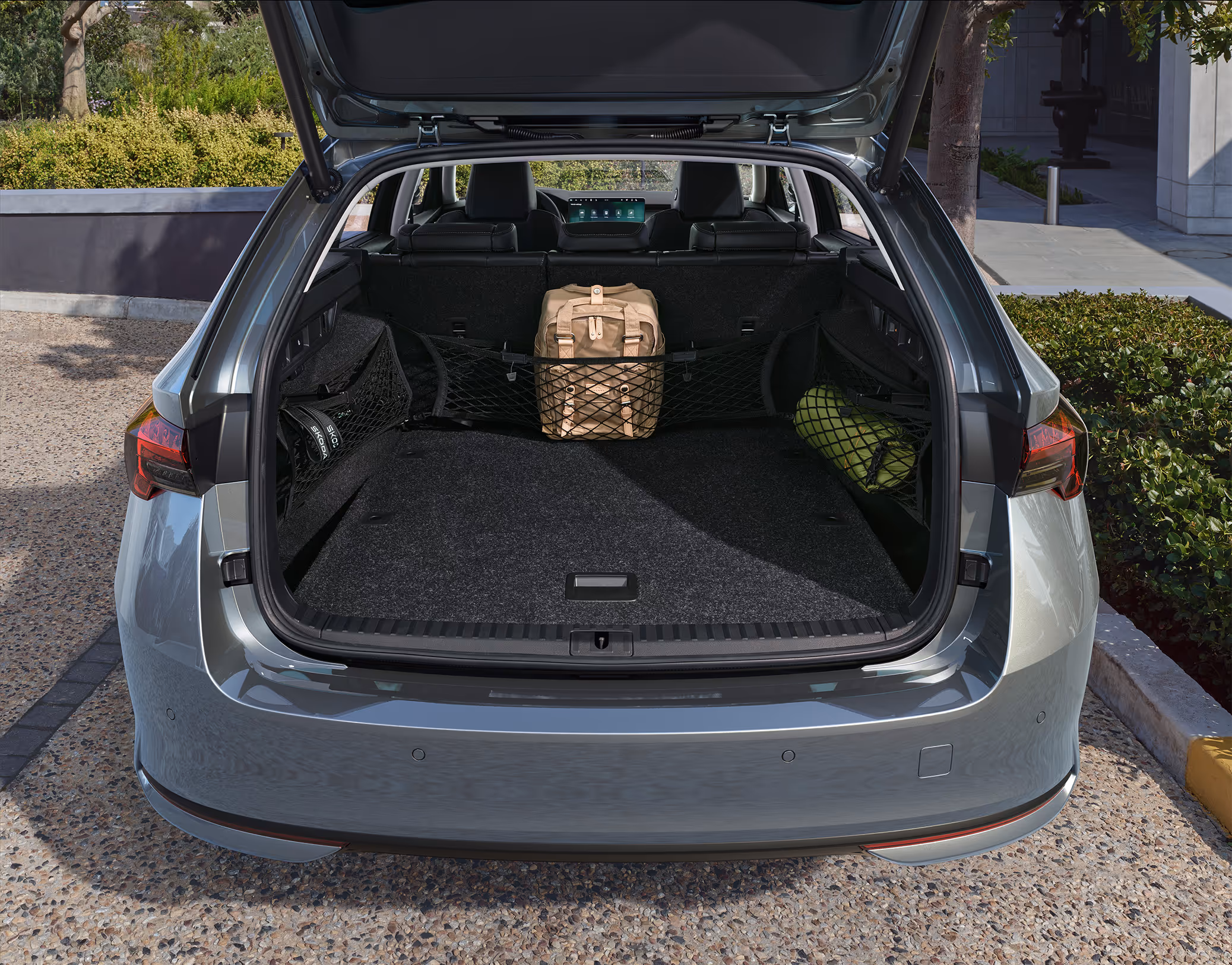 Eine Ansicht des geöffneten Kofferraums eines Škoda Octavia Combi zeigt die Anwendung des Netzprogramms. Ein beiger Rucksack wird von einem Netz hinter der Rücksitzlehne gehalten, während in seitlichen Netzen weitere Gegenstände wie eine grüne, gerollte Matte verstaut sind. Der Blick durch den Kofferraum nach vorne zeigt das Cockpit des Fahrzeugs.