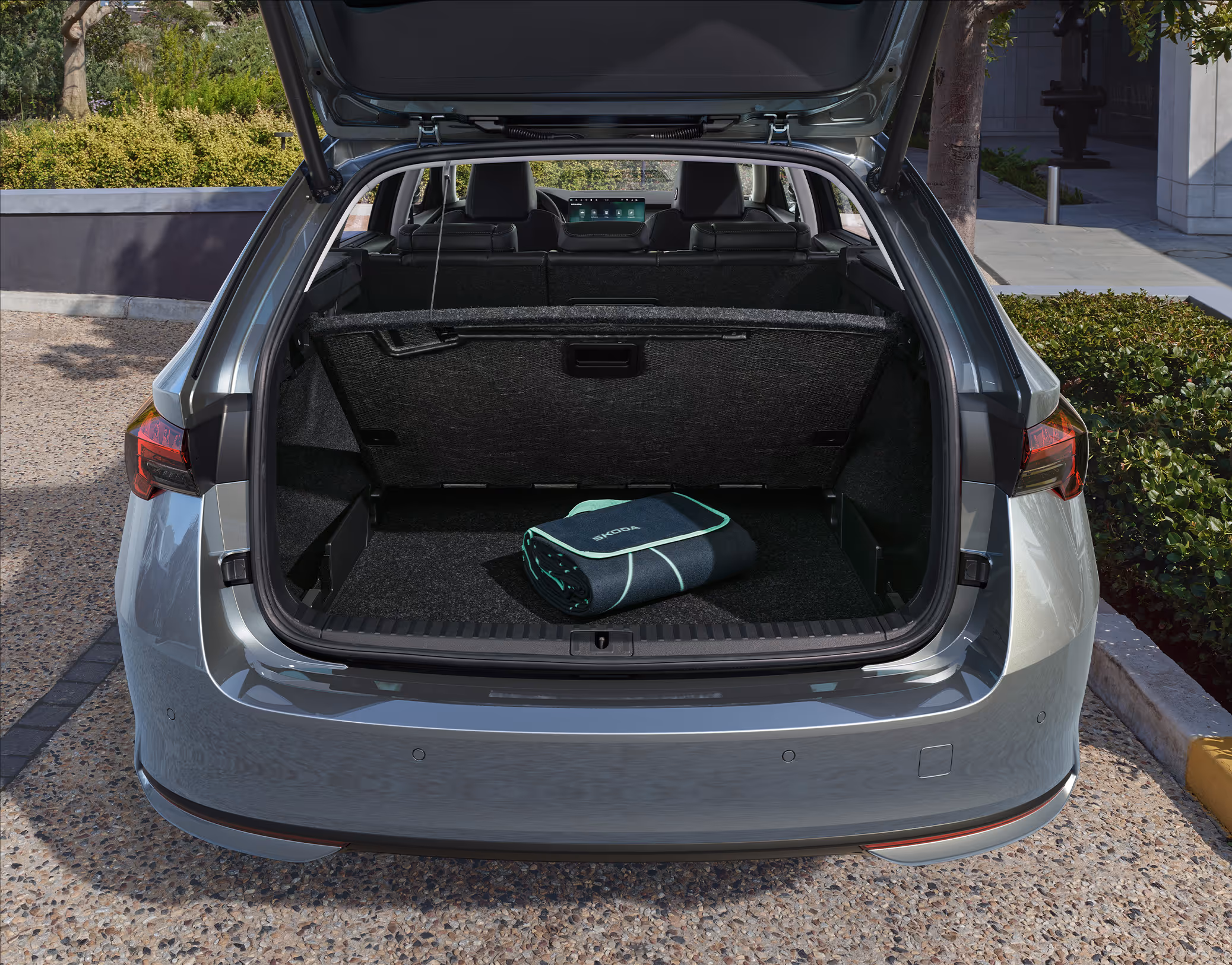 Eine Ansicht des geöffneten Kofferraums eines Škoda Octavia Combi zeigt eine zusammengelegte Ladekabeltasche auf dem Kofferraumboden. Darüber ist die hochgeklappte Kofferraumabdeckung zu sehen, während der Blick nach vorne zum Cockpit des Fahrzeugs reicht.

