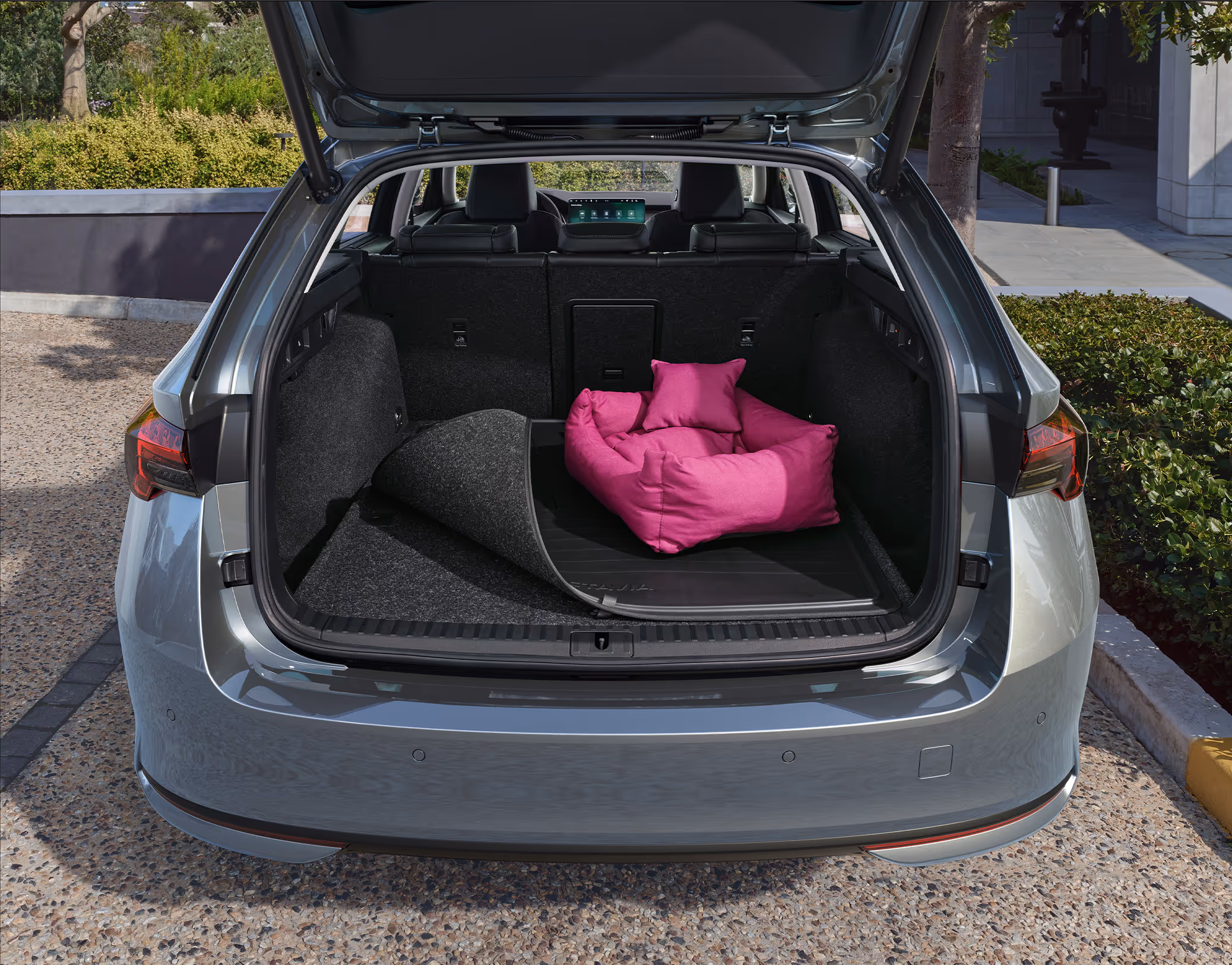 Eine Ansicht des geöffneten Kofferraums eines Škoda Octavia Combi zeigt eine doppelseitige Kofferraummatte, die teilweise umgeschlagen ist, um die Gummiseite freizulegen. Auf der Gummimatte steht ein großes, pinkes Hundebett.